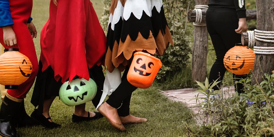 lower half of kids in halloween costumes carrying pumpkin buckets
